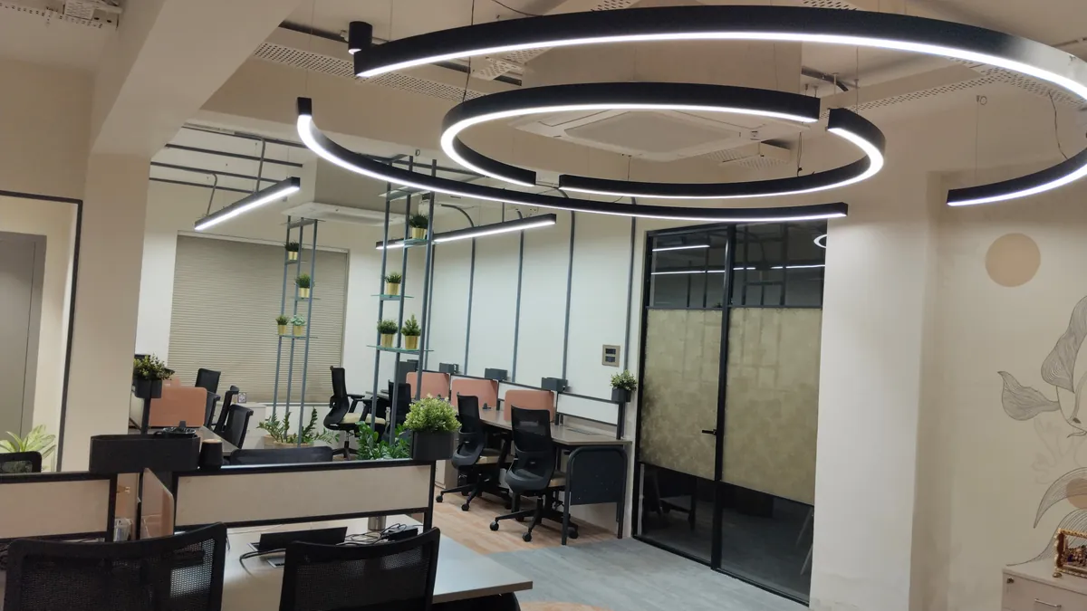 Open-plan office with black ring pendant lights, workstations and a glass partition
