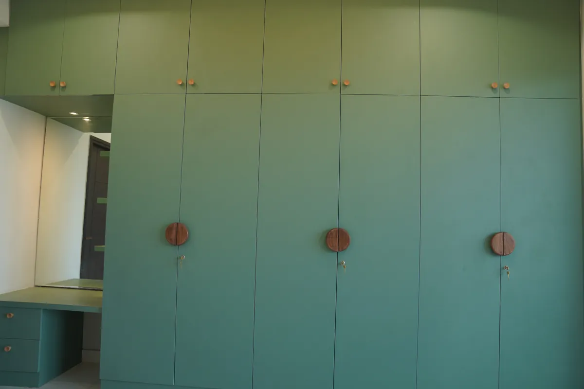 Full-wall sage green wardrobe with round walnut handles and dressing corner